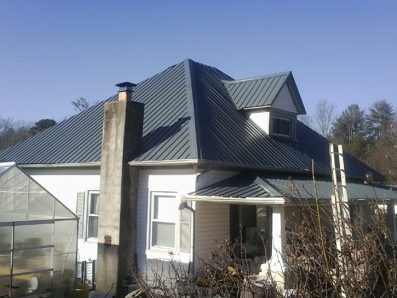 Dark blue standing seam metal roof on a white farmhouse with dormer — Slate & Tile Roof Repair by Roofing Brothers in Mercer